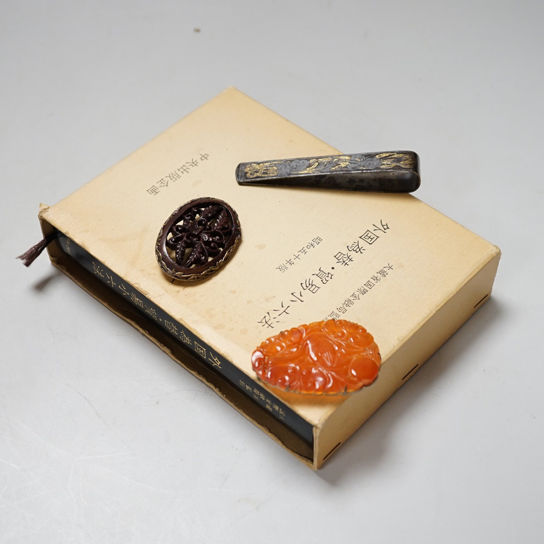 A Chinese chalcedony brooch, a Chinese carved wood brooch, a damascened steel clip and a Japanese trade reference book